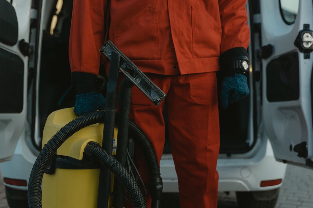 hero-02 A professional cleaner in a red uniform holding a vacuum near a van, ready for service.